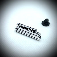 An enamel pin saying thinking…