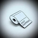An enamel pin of toilet paper roll saying shit happens